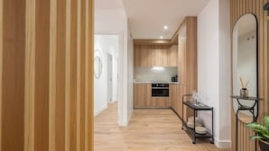A modern kitchen with wooden cabinets, a black countertop, and a small dining area with a table and chairs. - Apartamentos Príncipe de Canalejas (Ma)