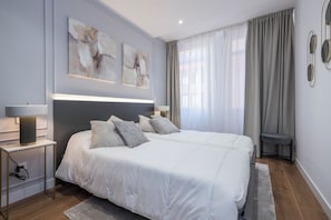 A modern bedroom with a large bed, bedside lamps, abstract wall art, and a view of the outdoors through sheer curtains. - Apartamentos Príncipe de Canalejas (Ma)