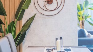 A dining area with a table set for two, a wall-mounted clock, and a hanging light fixture. - Apartamentos Príncipe de Canalejas (Ma)