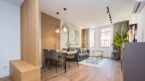 A modern living room with a dining area, wooden paneling, and a large window. - Apartamentos Príncipe de Canalejas (Ma)