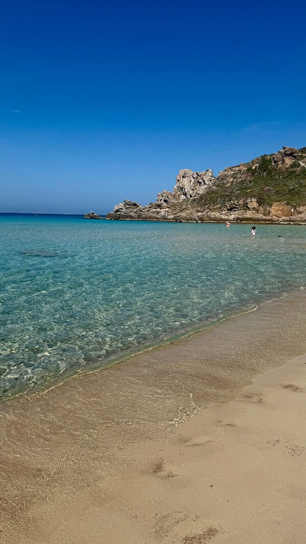 A beach with clear water, a sandy shore, and rocky cliffs.