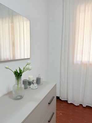 A bathroom with a white vanity, a mirror, a vase with flowers, and a window with curtains.