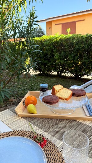 A wooden tray with food items, a glass, and a wicker basket on a table outdoors.