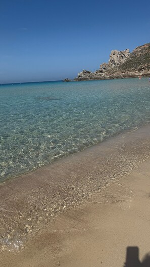 En strand med klart vatten, en klippformation och en avlägsen utsikt över havet.