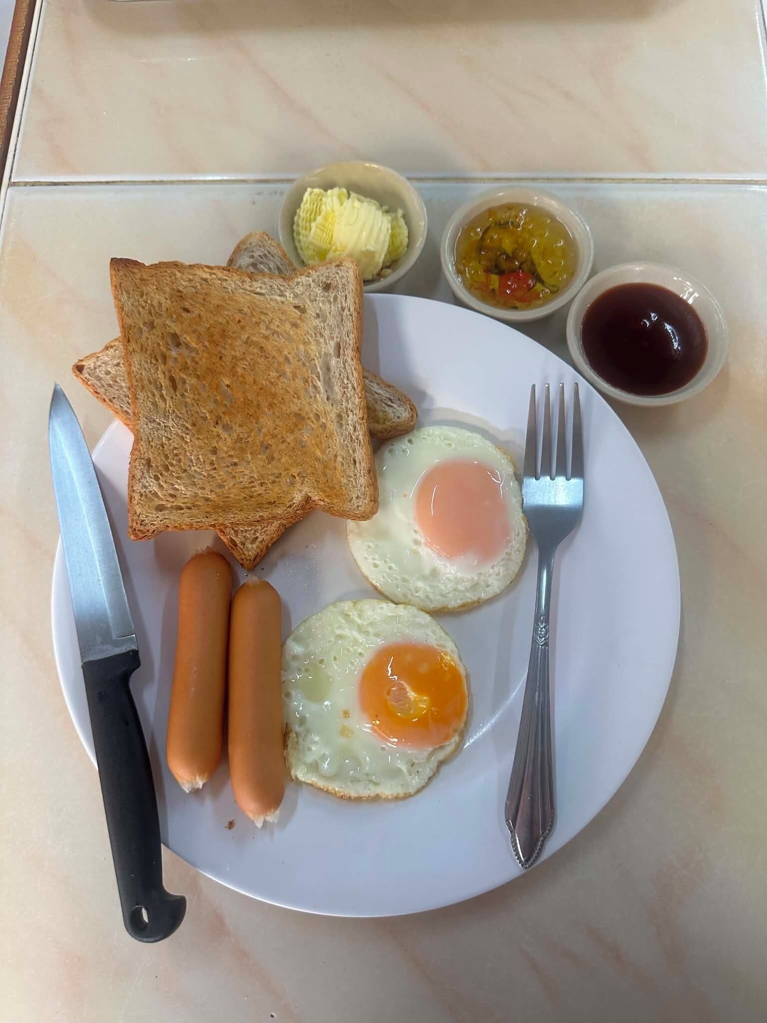 A plate with toast, two fried eggs, two sausages, and condiments.