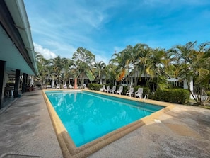 A swimming pool with lounge chairs, palm trees, and a building with a tiled floor. - SouanSonBeachResort (MUEANG RAYONG)
