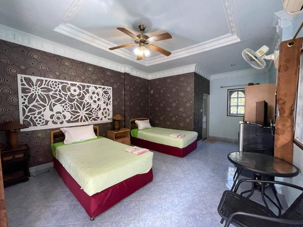 Ein Hotelzimmer mit zwei Betten, einem Deckenventilator, einem Schreibtisch mit Stuhl und einem Fenster.
