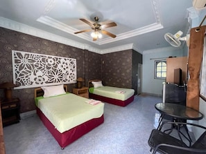 Ein Hotelzimmer mit zwei Betten, einem Deckenventilator, einem Schreibtisch mit Stuhl und einem Fenster.