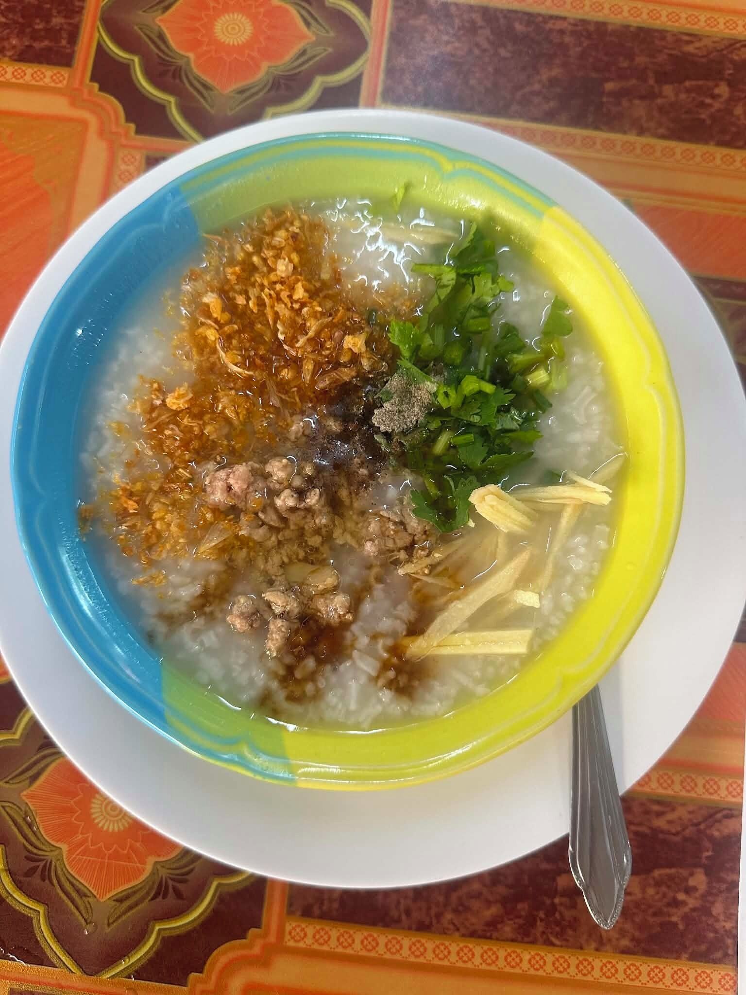 Uma tigela de papa de arroz com acompanhamentos, sobre uma toalha de mesa estampada.