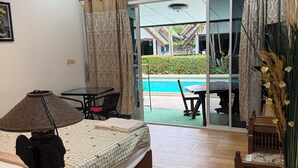 Habitación de hotel con cama, mesa, silla, lámpara y vista a una piscina.
