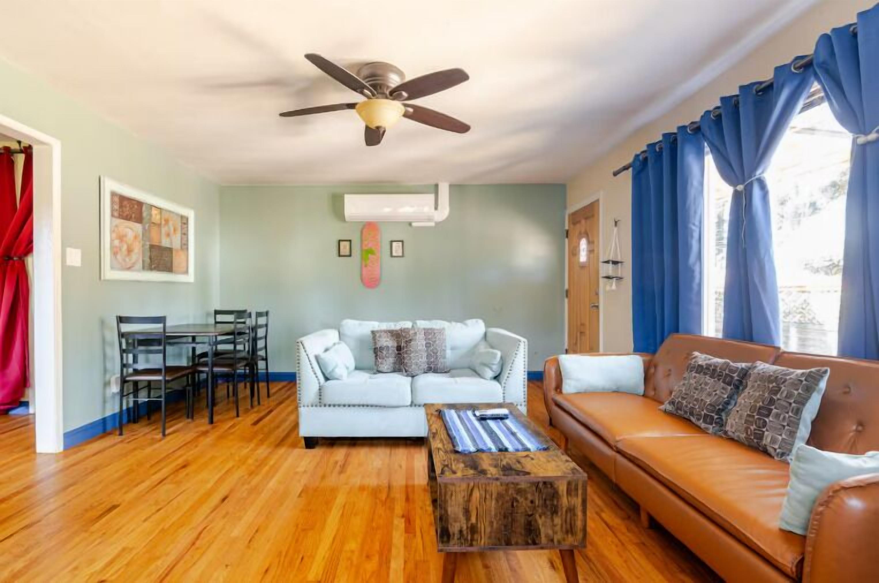 A living room with a ceiling fan, a dining table with chairs, a light blue sofa, a brown sofa, and a wooden coffee table.