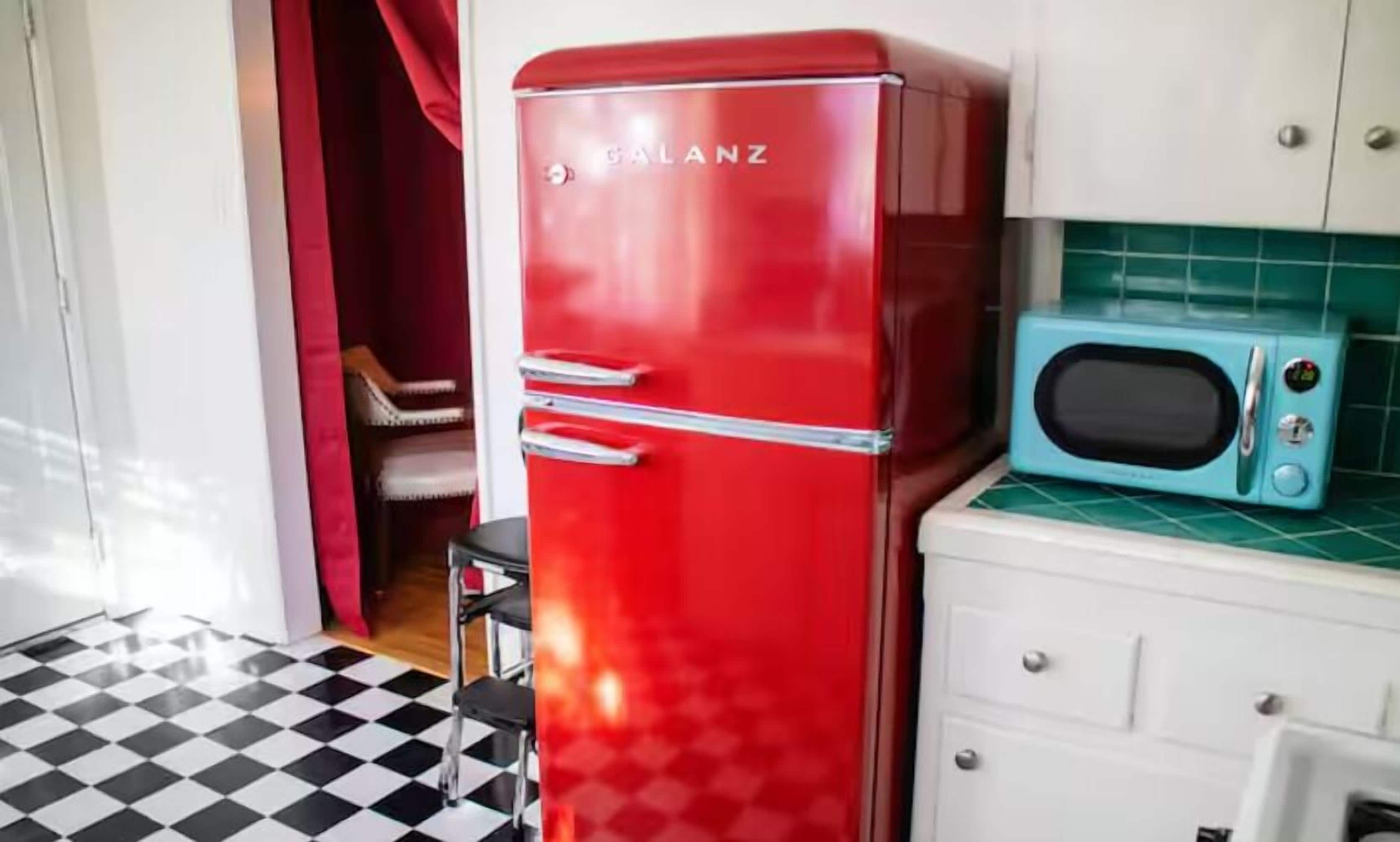 Ein roter Kühlschrank, eine blaue Mikrowelle und ein weißes Schränkchen in einer Küche mit kariertem Boden.