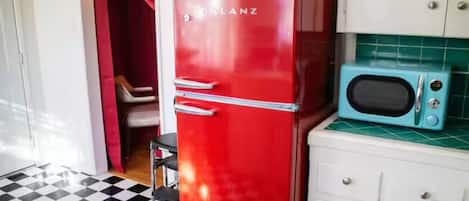 Ein roter Kühlschrank, eine blaue Mikrowelle und ein weißes Schränkchen in einer Küche mit kariertem Boden.