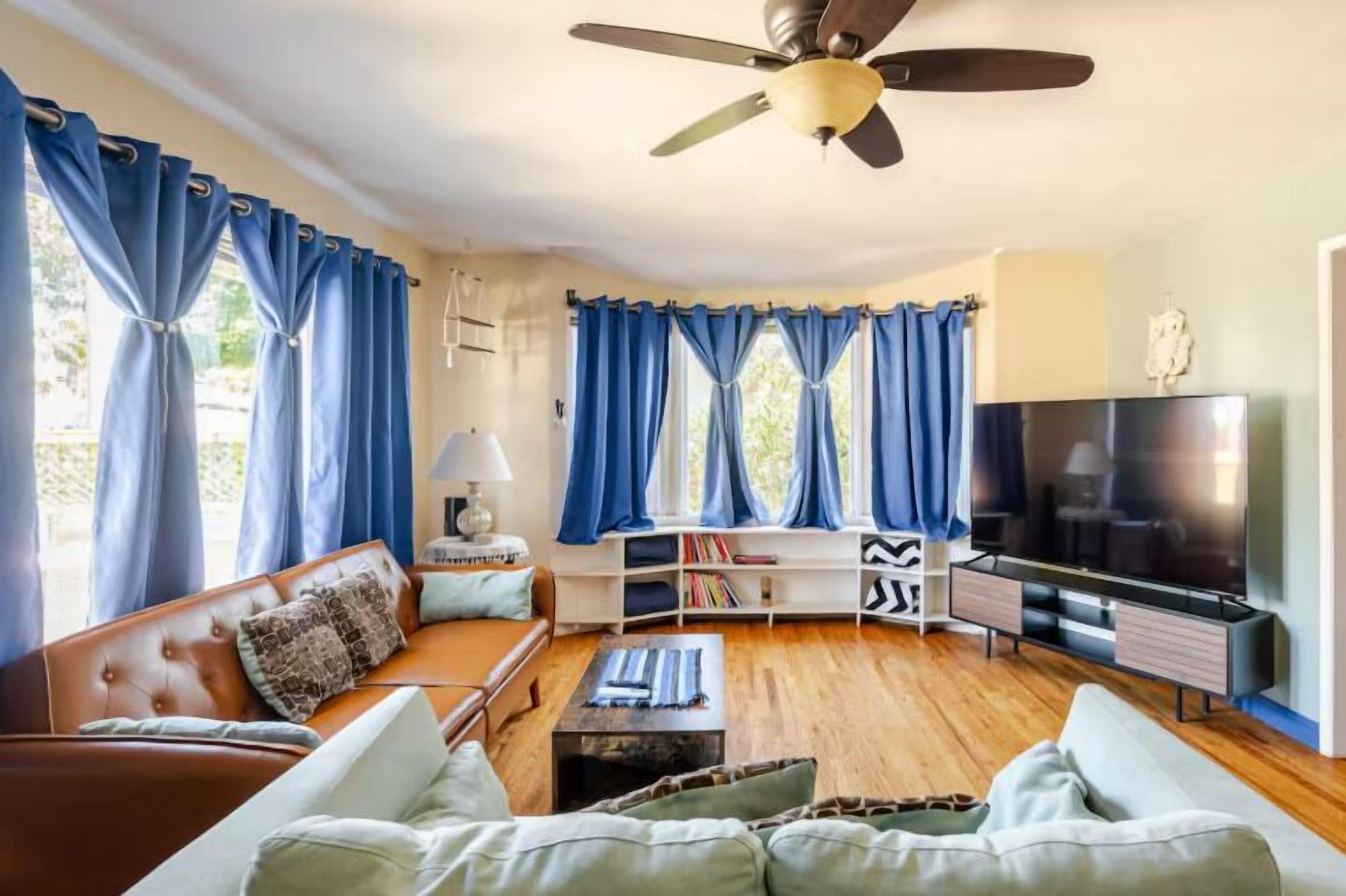 Een woonkamer met een bank, televisie en een plafondventilator.