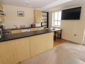 A modern kitchen with a central island, wooden cabinets, a built-in oven, and a dining area with a table and chairs. - Twyni Bach (Burry Port)
