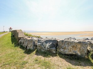 Ein Küstenpfad mit Leuchtturm, Felsen und Sandstrand.