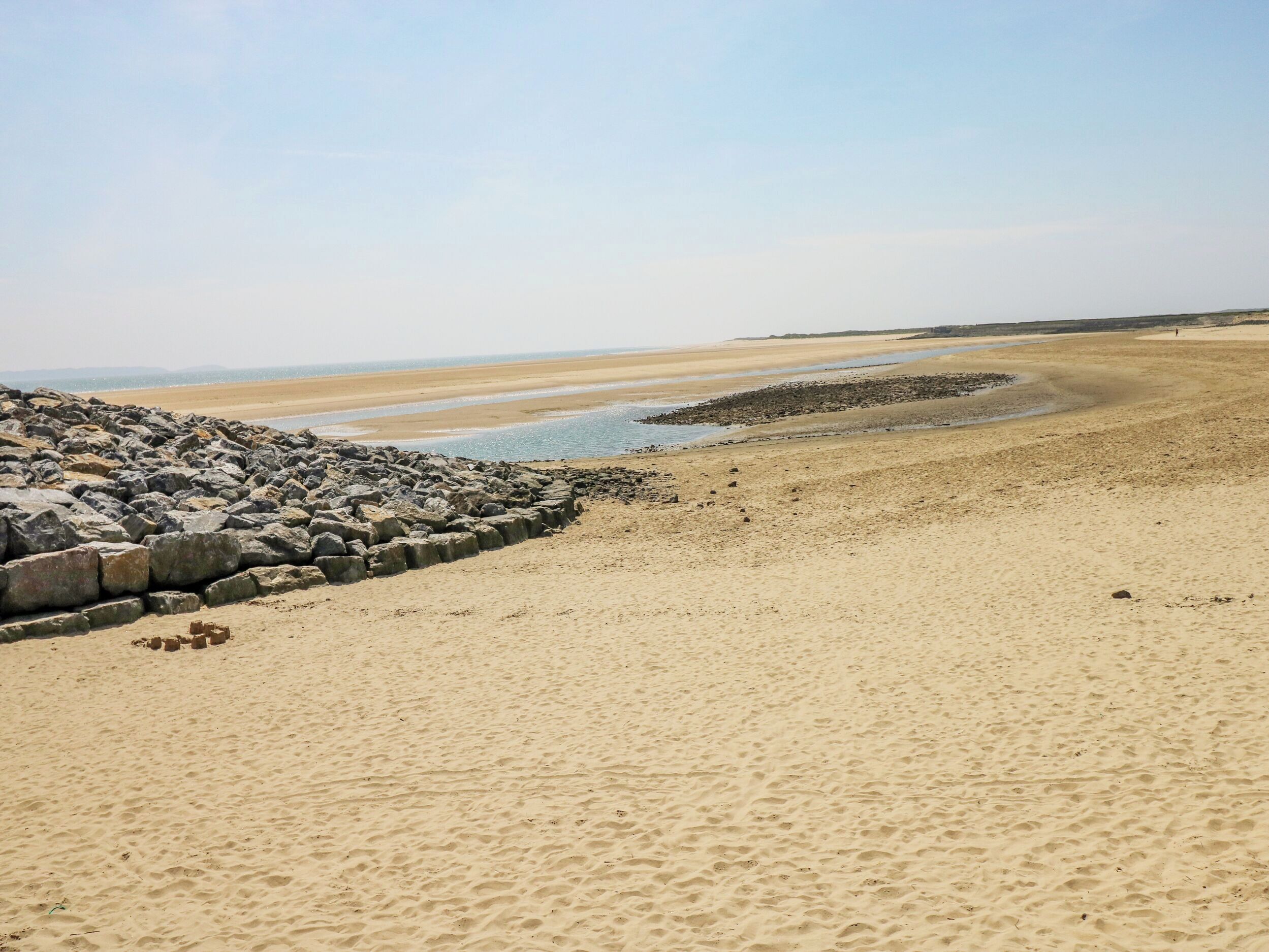 A beach with a rocky breakwater and a sandy shore.
