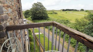 Ein Balkon mit Steinmauer, Metallgeländer und Blick auf eine grüne Landschaft.