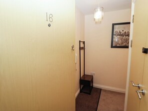 A hallway with a door marked '16', a coat rack, a framed picture on the wall, and a carpeted floor. - Twyni Bach (Burry Port)
