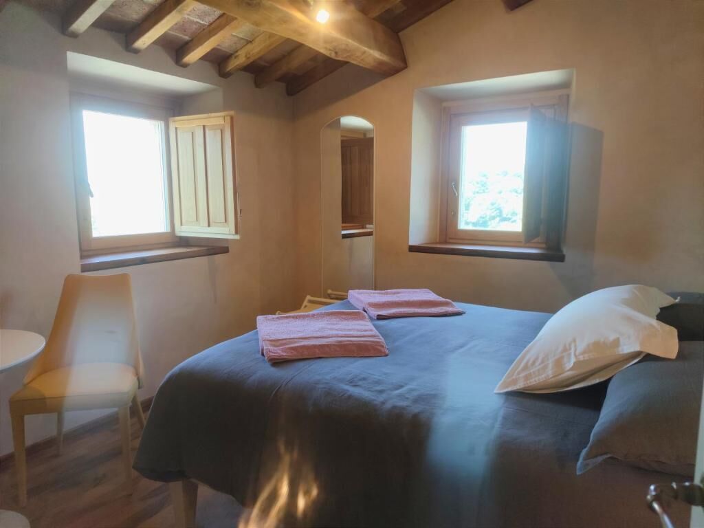 A bedroom with a bed, two windows, a chair, and a small table.