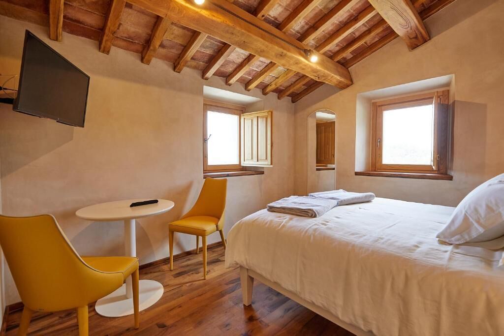 A bedroom with a bed, a chair, a small table, and a TV mounted on the wall.