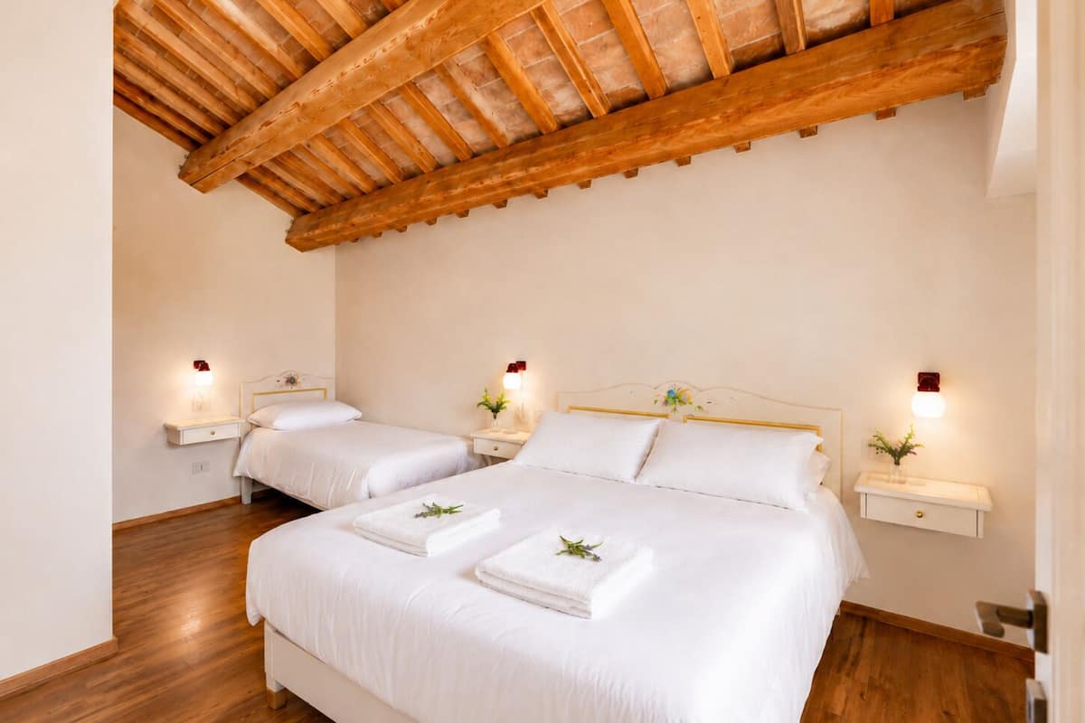 Una habitación de hotel con dos camas, suelo de madera, techo inclinado y lámparas de noche.