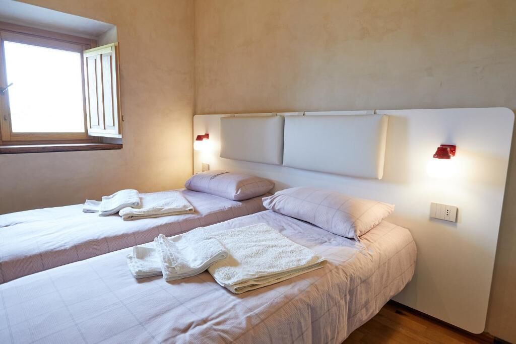 Habitación de hotel con dos camas, una ventana y luces fijadas a la pared.