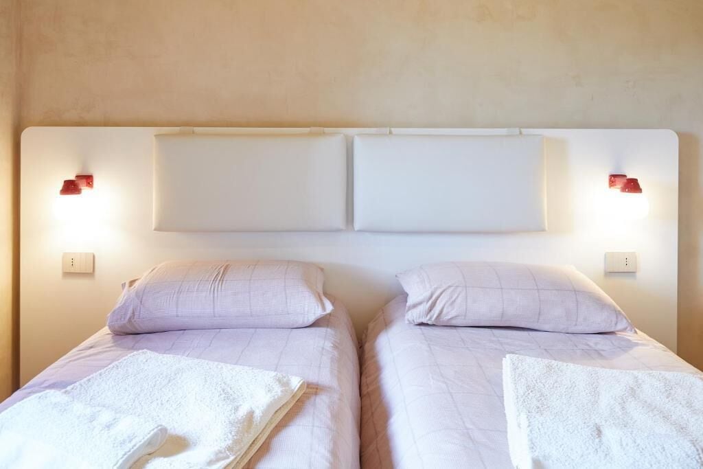 Un letto matrimoniale con due cuscini e una coperta bianca, due abat-jour e una parete semplice.