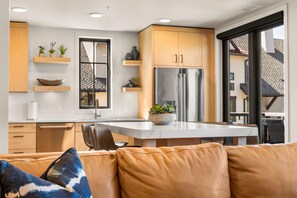 A modern kitchen with a central island, wooden cabinets, and a stainless steel refrigerator. - The Nest | Exclusive Tamarack Perks (Tamarack)