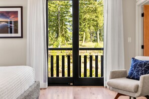 A room with a bed, a chair, a door, and a view of a forest through a glass door. - The Nest | Exclusive Tamarack Perks (Tamarack)