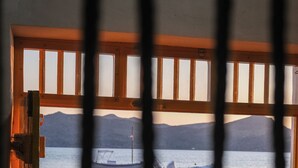A view through a window with wooden frames, featuring boats on the water and a mountainous landscape in the background. - Rota Klima (Milos)