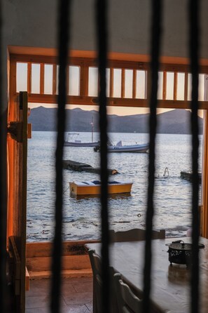 A view through a window with wooden frames, featuring boats on the water and a mountainous landscape in the background. - Rota Klima (Milos)