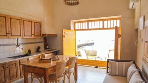 A kitchen with wooden cabinets, a dining table with chairs, and a view through a large window. - Rota Klima (Milos)