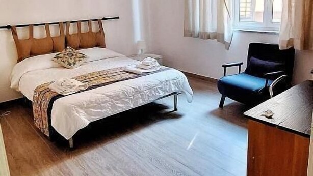 Ein Schlafzimmer mit einem Bett, einem Schreibtisch, einem Stuhl, einer Pendelleuchte und einem Fenster mit Vorhängen.
