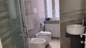 Ein modernes Badezimmer mit Duschkabine aus Glas, einem Bidet, einem Waschbecken und einer Toilette.