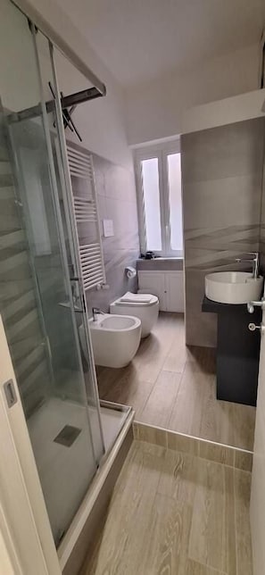 A modern bathroom with a glass shower enclosure, a bidet, a sink, and a toilet. - A casa di Giulia (Palermo)