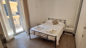 Ein Schlafzimmer mit Bett, Nachttischen, einem Fenster mit Vorhängen und einer Tür.