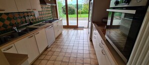Une cuisine équipée d’une cuisinière à gaz, d’un four et offrant une vue sur l’extérieur grâce à une porte coulissante.