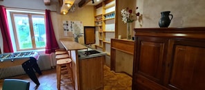 Une cuisine avec un bar en bois, des tabourets, une table de baby-foot et une vue à travers une porte vitrée.