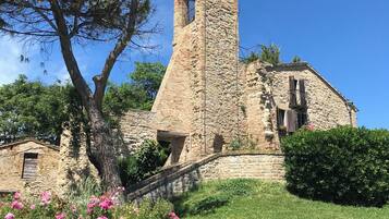 Une église en pierre dotée d’un clocher, entourée de verdure et de plantes en fleurs.