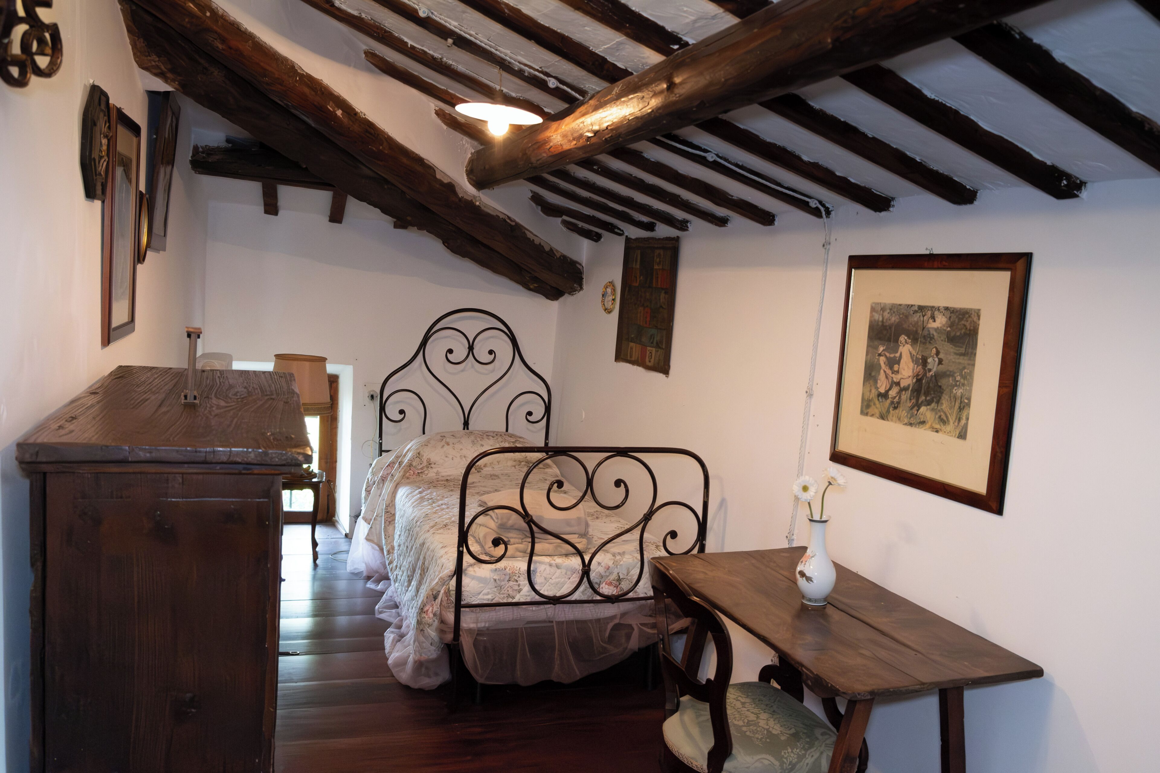 A bedroom with a wooden bed, a wooden nightstand, a small table, and a wall-mounted picture.