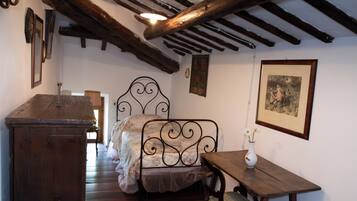 A bedroom with a wooden bed, a wooden nightstand, a small table, and a wall-mounted picture.