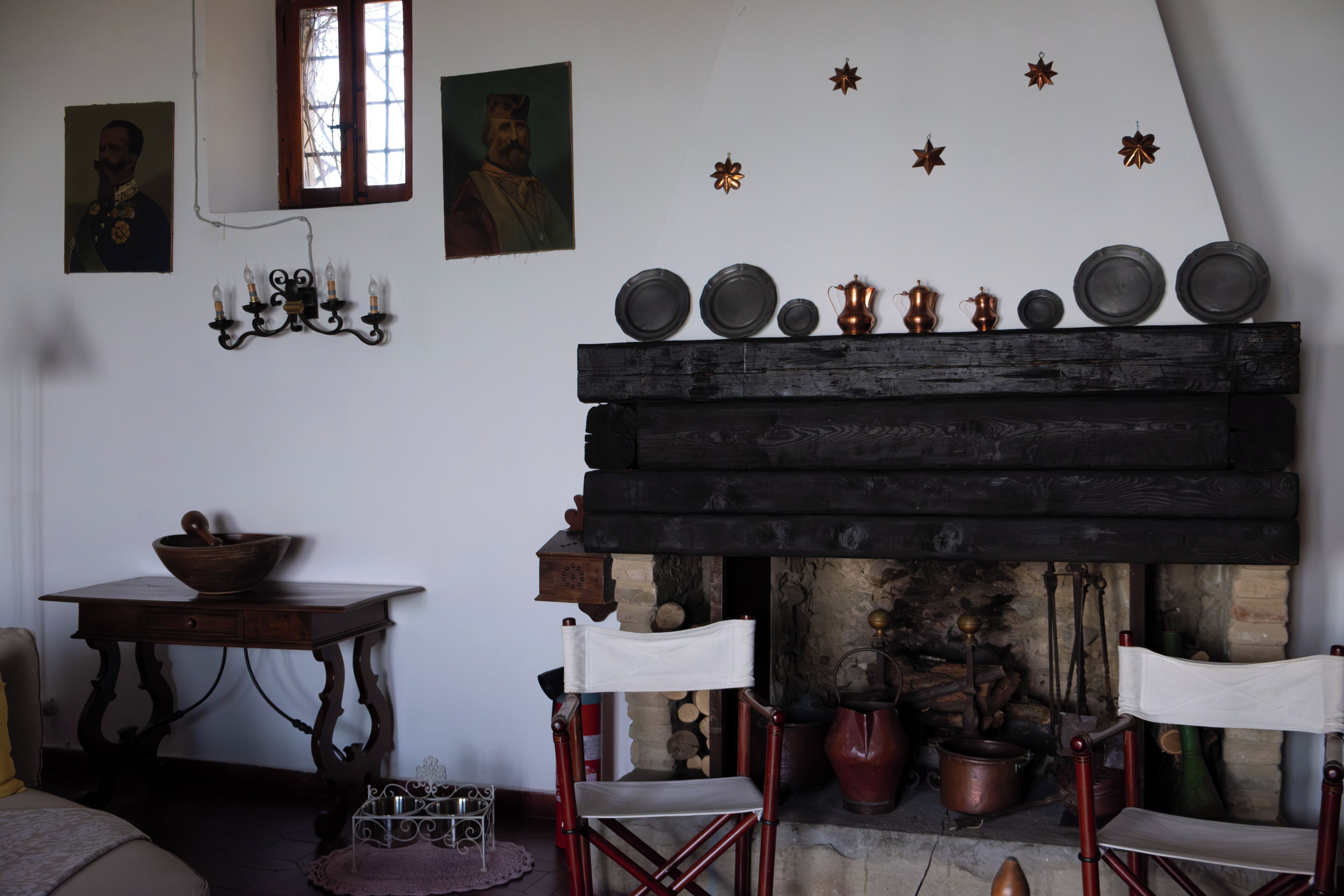 Une pièce avec une cheminée, une table sur laquelle se trouve un bol, deux chaises, ainsi que des assiettes et des décorations en forme d’étoiles accrochées au mur.