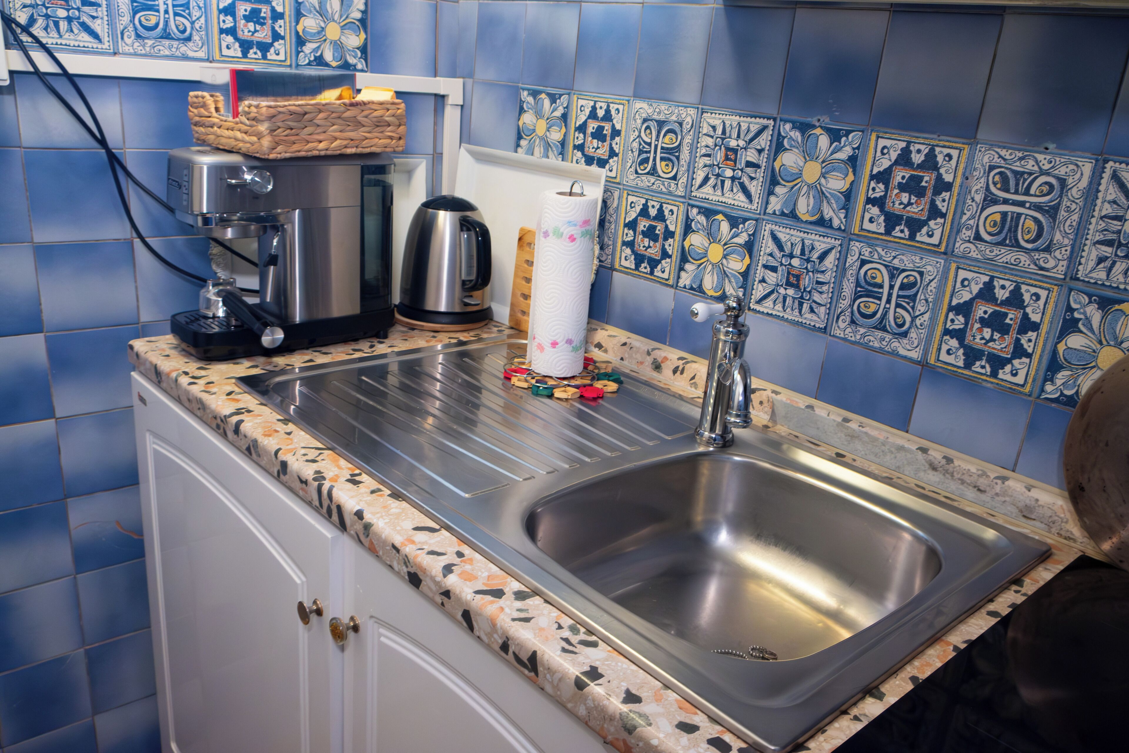 A kitchen with a stainless steel sink, a coffee maker, and a kettle on the counter.