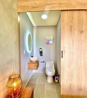 A bathroom with a wooden vanity, a round mirror, a toilet, and a small shelf with a towel. - Listing With Bookings, Messages abc (Pattaya)