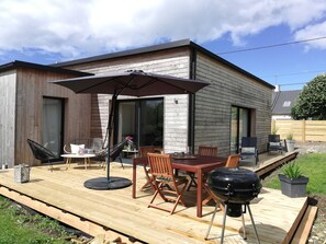 Ein modernes Haus mit Terrasse, Sitzgelegenheiten im Freien, Grill und einem großen Sonnenschirm.