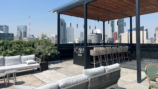 Tagbar med siddepladser, udsigt over byens skyline, og et skilt med teksten 'ICON BAR'.
