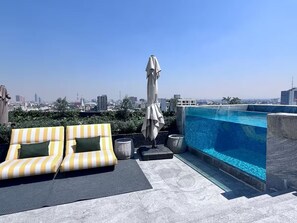 A rooftop pool area with two striped lounge chairs, a covered umbrella, and a view of the cityscape. - Design Loft - ICON Roma - Rooftop Pool + Bar - Heart of CDMX (Ciudad de México)