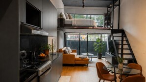 Et moderne køkken med indbygget komfur, et spiseområde med et glasbord, og et sovehems med seng.