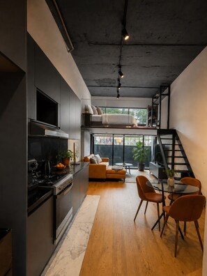 A modern kitchen with a built-in stove, a dining area with a glass table, and a loft bedroom with a bed. - Design Loft - ICON Roma - Rooftop Pool + Bar - Heart of CDMX (Ciudad de México)